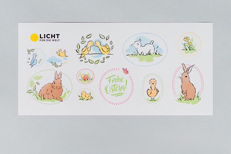 Aufkleber mit Osterillustrationen für Licht für die Welt: 1 Schaf, 2 Hasen, 2 Küken, 2 Vögel einander zugewandt, 2 kleinere Vögel, bunte Eier im Gras, zwei gelbe Blümchen + 1 mal "Frohe Ostern" mit einem Schmetterling